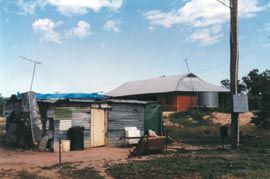 A humpy retained as a past lifestyle symbol in a rural town in western New South Wales in 1999 with an ATSIC house behind. Photograph Paul Memmott.