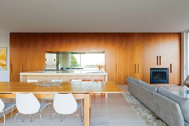 A stainless steel cooking zone is framed by the joinery and has a mirrored splashback that reflects a coastal view.