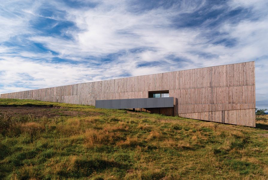 The geometric form of Marion Bay House is wrapped by a timber-clad wall that seems to disappear into the hill.