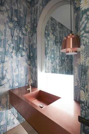 The distinctive powder room features wallpaper by Bethany Linz paired with a copper vanity and pendant.