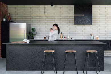 A kitchen in black oriented strand board (OSB) adds texture and tonal contrast to the white brick wall and light-filled courtyard opposite.