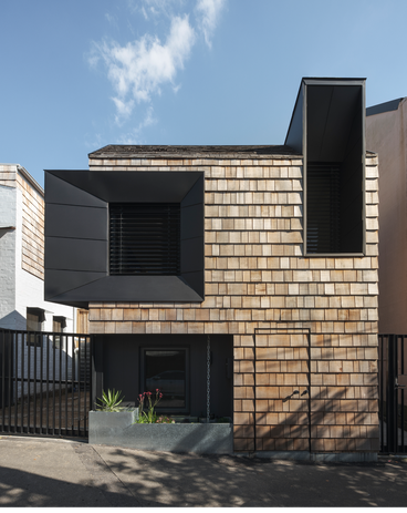 The facade is wrapped in cedar shingles and features two expressive window hoods that extend out and up.