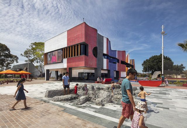 Visitors of all ages frolic in the striking and tactile water feature that foregrounds the hub building’s undulating and colourful west face.