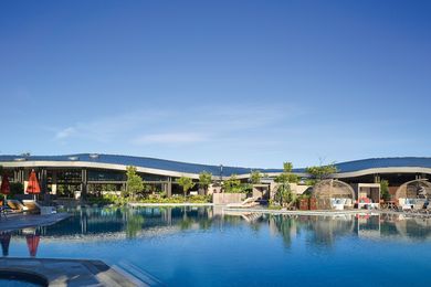 The crescent form of the double curved zinc roof opens up to a large pool, with views to vegetated sand dunes in the distance.