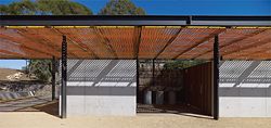 A solid concrete wall and tall doors of timber slats form the toilet pavilion. Image: Brett Boardman