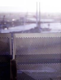 A folded perforated aluminium balcony, high up in Liberty Tower, with views west across Docklands, freeway infrastructure, and out to Port Phillip Bay.