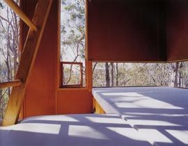 Interior view, with ground level sleeping areas and the ladder to the upper level sleeping area. Horizontal and vertical windows frame the landscape and sky.