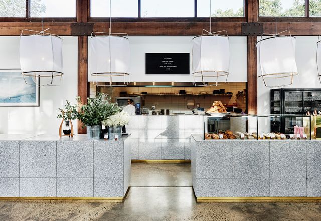 The bar and counter frame the open kitchen and feature speckled grey terrazzo and floating white pendant lights.