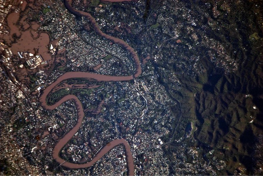 This detailed satellite photograph illustrates flooding in metropolitan suburbs of the Brisbane, Queensland, Australia. Please note that the top of the photo is oriented approximately to the South-West and not to the North. The image, taken by astronauts on board the International Space Station, highlights several suburbs along the Brisbane River in the southern part of the Brisbane metropolitan area. The light-coloured rooftops of residences and other structures contrast sharply with green vegetation and brown, sediment laden flood-waters. Most visible low-lying areas are inundated by flood-water, perhaps the most striking being Rocklea at image upper left. The suburb of Yeronga (image lower left) also has evident regions of flooding, as does a park and golf course located along a bend in the Brisbane River to the south of St. Lucia (image center). Flooding becomes less apparent near the higher elevations of Mt. Coot-Tha at image right.  by ISS Expedition 26 crew