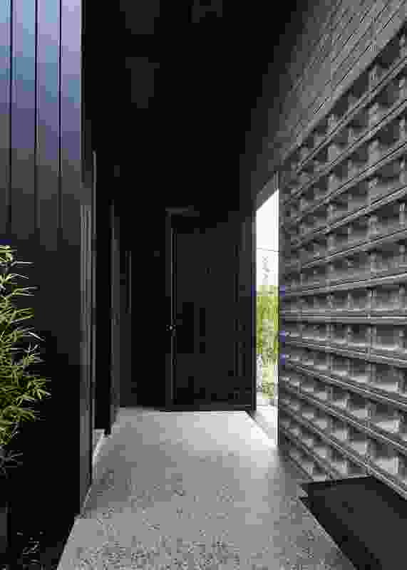 The front door is set within a portico behind a black steel gate and hollow concrete blocks.