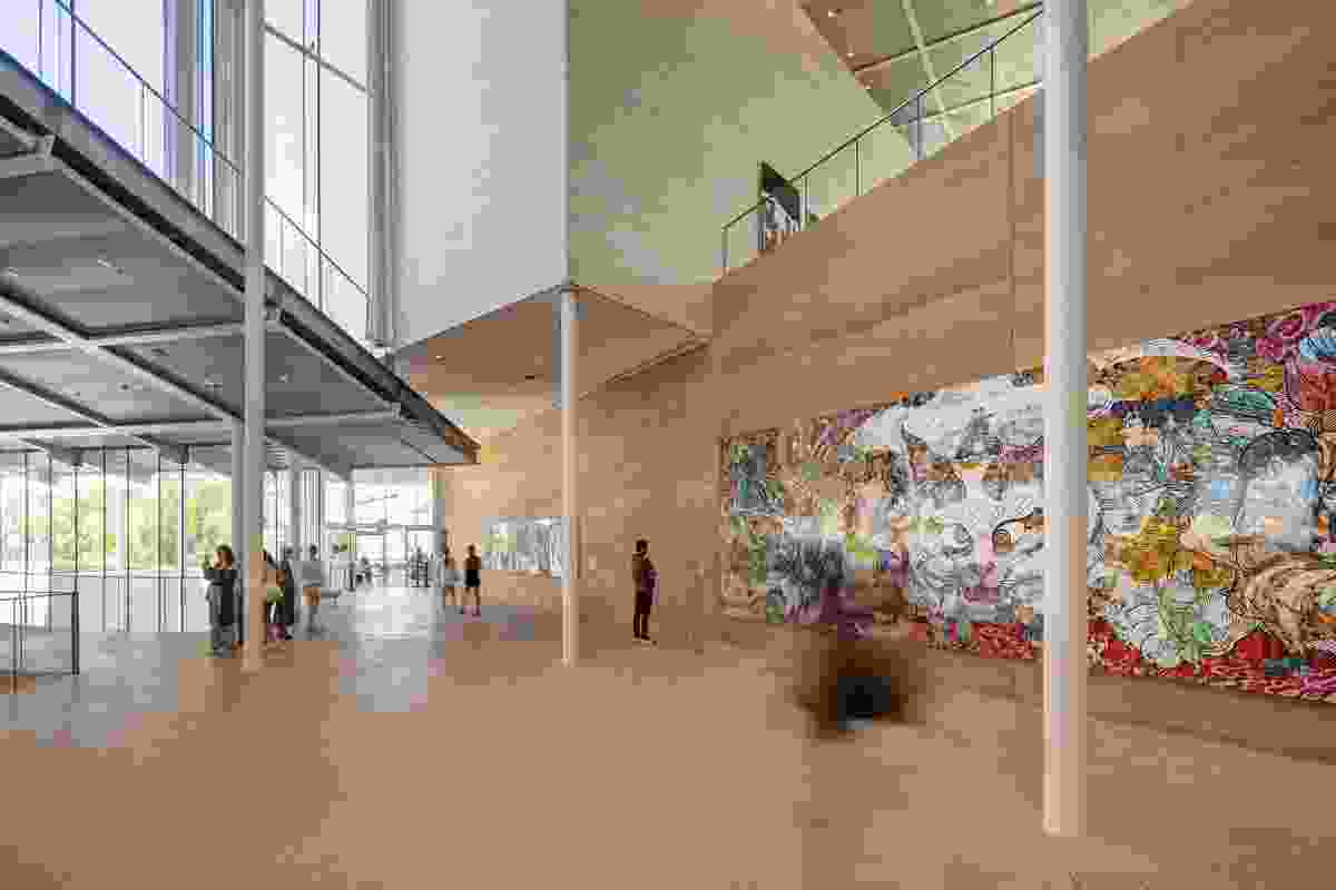 A rammed-earth feature wall, made from local sand, arcs through both the interior and exterior of the building. Artwork (L–R): Richard Lewer, Takashi Murakami/Kaikai Kiki Co., Ltd.