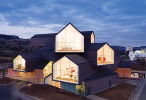 Elevated above the Vitra Campus in Germany, the building form is made up of a series of stacked, long, gabled roof telescopes.