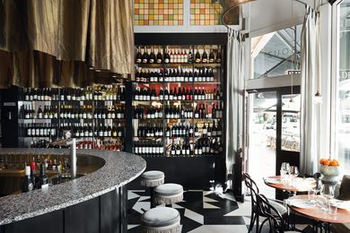 The space is layered with texture and detail, from the speckled terrazzo horseshoe-shaped bar to the tassels on the stools and the monochrome patterned floor.