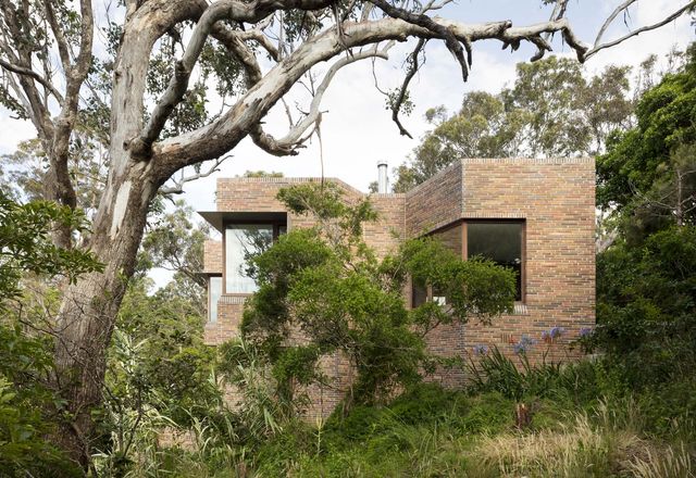 The slopes and folds of the house’s protective brick wall respond to the site’s steep topography.